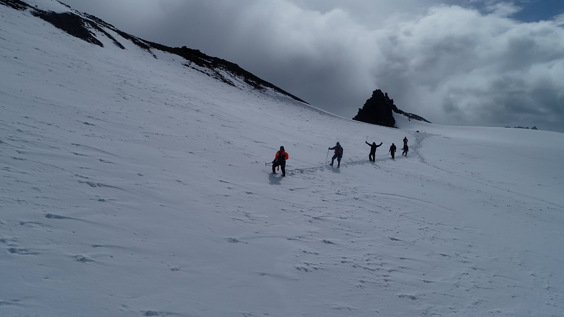 Three researchers in red jackets roped together, traversing the glacier surface on foot
